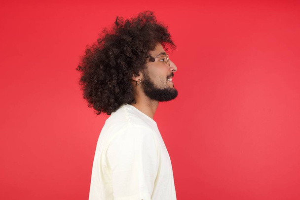 Jeune homme aux cheveux afro contre le mur rouge, vue latérale - Photo, image
