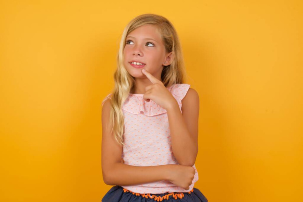 cute  little girl in pink dress against yellow studio background looking away  - Foto, imagen