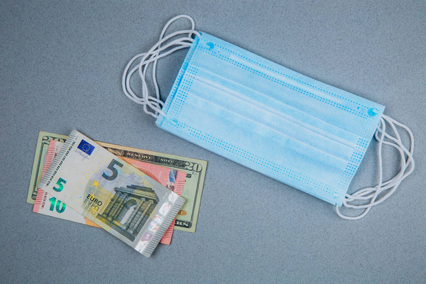 Ιατρική μάσκα και χρήματα.Ιατρική μάσκα κοντά σε δολάρια και ευρώ, Έννοια της αύξησης του κόστους για την προστασία του ιού. - Φωτογραφία, εικόνα
