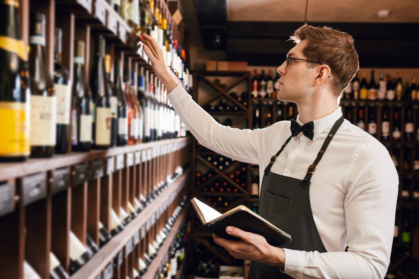 Sommelier writes at notes, putting down information on wine products in cellar - Фото, изображение