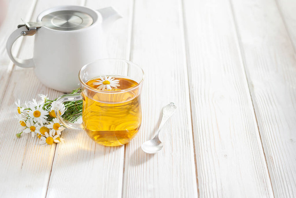 Cup of herbal tea with chamomile flowers on the white wooden background. Natural organic alternative medicine concept - Фото, зображення