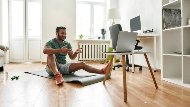 Motivate. Male fitness instructor explaining exercises while streaming, broadcasting video lesson on training at home using laptop. Sport, online gym concept - 写真・画像