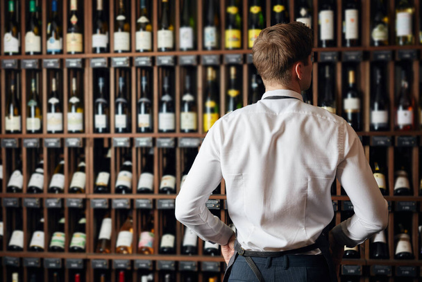 Backside of elegant wine seller selecting wine for customers in wine shop - Foto, Imagem
