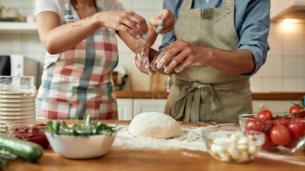 Cropped shot of couple preparing the dough together. Young man and woman in apron cooking, making pizza at home. Hobby, lifestyle - Foto, imagen