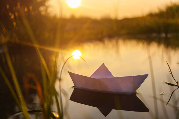 Um barco de papel flutua na água ao amanhecer. Conceito criativo de recreação ao ar livre, rio, viagens. Imagem bonito acolhedor em cores quentes. Espaço de cópia. - Foto, Imagem