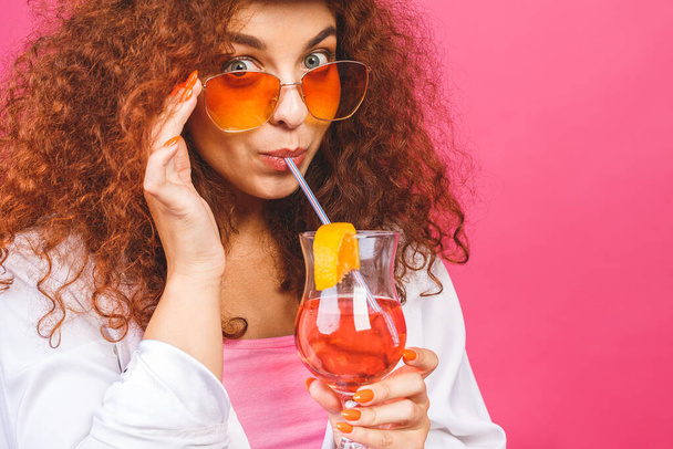 Mutlu güzel kadın yaz kıyafetleri içinde bir bardak kokteyl içeceği stüdyosuyla renkli pembe arka planda izole edilmiş.. - Fotoğraf, Görsel