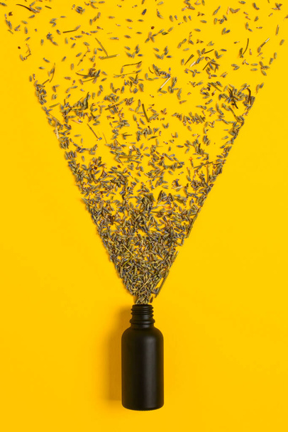cosmetic black matte glass dropper bottle on a yellow background. Lavender flowers scatter like small droplets from a spray. flat lay. - Foto, Imagen