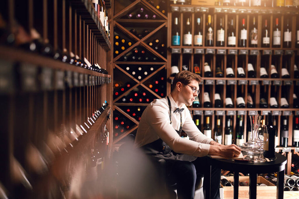 Sommelier writes at notes, putting down information on wine products in cellar - Photo, image