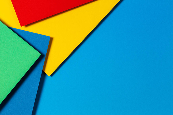 Absztrakt színes papírok geometria lapos feküdt kompozíció háttér kék, sárga, zöld és piros színű tónusok - Fotó, kép
