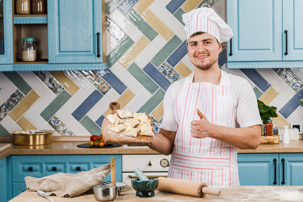 Kuchař v kuchyni drží v rukou knedlíky a ukazuje na ně rukou. Koncept vaření - Fotografie, Obrázek