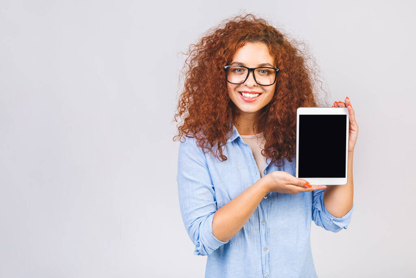Kuva iloinen hämmästynyt nuori kihara valkoihoinen nainen näyttää tabletin tietokoneen. Digitaalinen tabletin näyttö eristetty valkoisella taustalla. - Valokuva, kuva