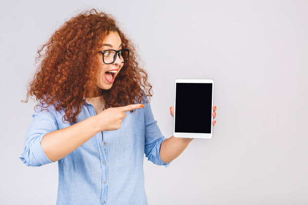 Happy winner. Image of cheerful amazed young curly caucasian woman showing display of tablet computer. Digital tablet screen isolated over white background. - Foto, afbeelding