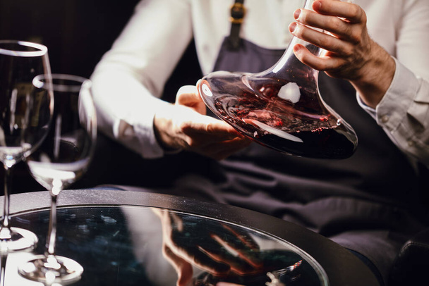 Сомелье наливает красное вино из бутылки в графин за столом в ресторане - Фото, изображение