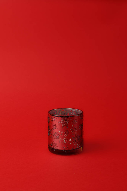 glass candlestick with ornament of snowflakes on a red background. Vertical photo. Copy space. Christmas concept. Minimalism. - Valokuva, kuva