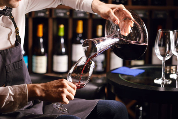 Skilled sommelier pouring wine from decanter ino wine glass. - 写真・画像