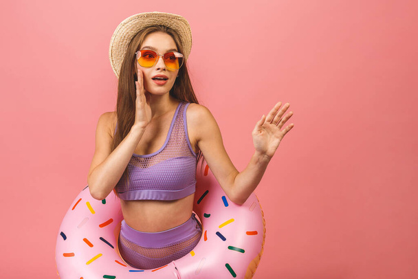 Portrait of a happy young woman dressed in swimsuit jumping and holding swim inflatable ring isolated over pink background. - Photo, image