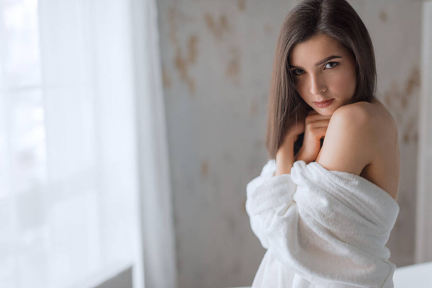 Brown-haired woman in bathrobe, posing with bare shoulders next to bath tube - Фото, зображення