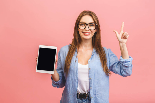 Casual χαμογελώντας γυναίκα των επιχειρήσεων δείχνει κενή οθόνη του υπολογιστή tablet πάνω από ροζ φόντο. Κοιτάζοντας την κάμερα. - Φωτογραφία, εικόνα