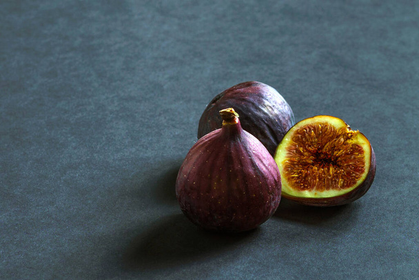 Three ripe figs on a gray background. One is cut in half. - Photo, Image