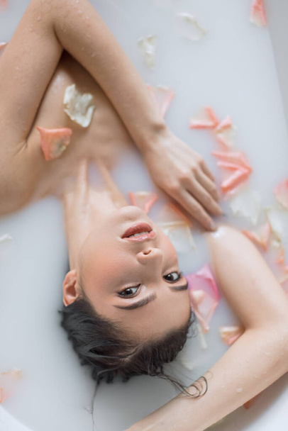 Young woman takes a milk aroma bath with flower petals - 写真・画像