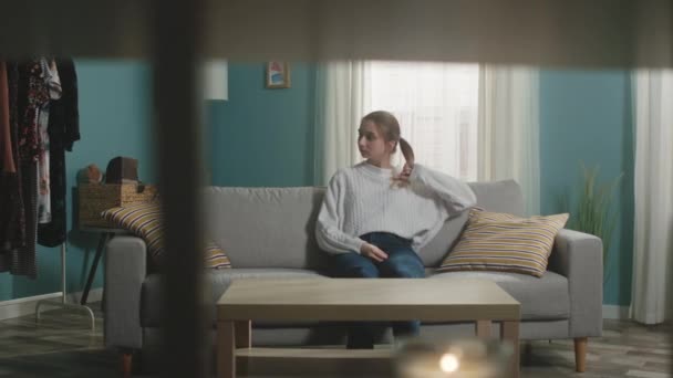 Chica joven con el pelo rubio se sienta en el sofá delante de la mesa y sacude la cabeza - Metraje, vídeo