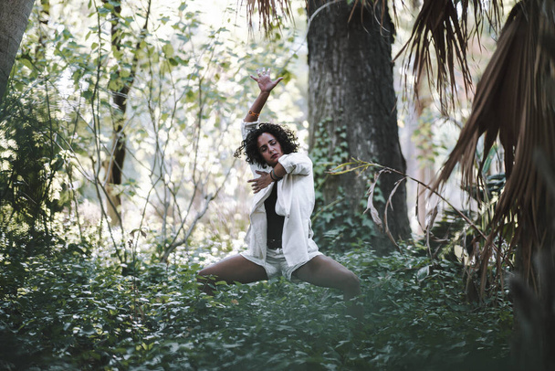A young caucasian curly female posing in the forest with expressive movements - Fotografie, Obrázek