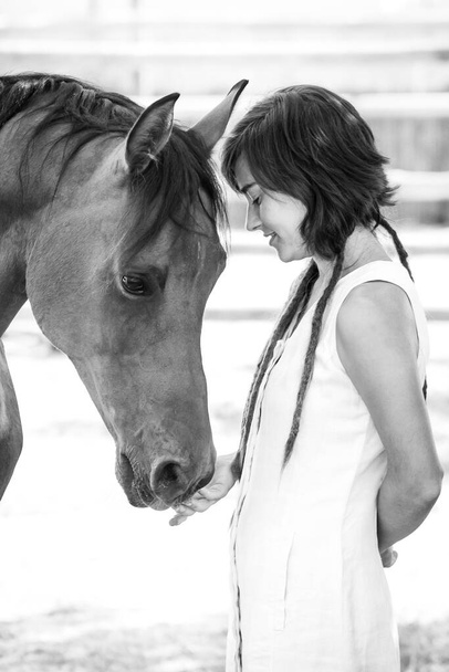 Ασπρόμαυρη εικόνα ενός κοριτσιού που φροντίζει και χαϊδεύει ένα αραβικό άλογο ράτσας. - Φωτογραφία, εικόνα