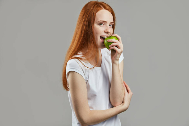 awesome girl with long red hair is eating a green apple - Foto, Bild