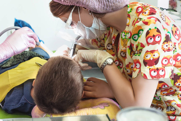 Молодая женщина-стоматолог в маске с оборудованием в руках работает в стоматологической клинике. Здравоохранение и стоматологическое лечение - Фото, изображение