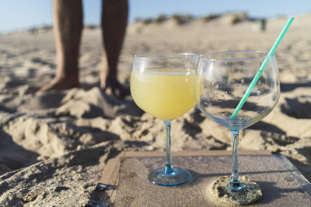 A closeup shot of a glass filled with a cocktail and an empty one at the beach - Foto, Imagem