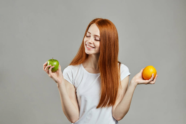 smiling cheerful girl comparing apple and orange - Valokuva, kuva
