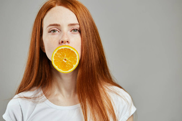gorgeous girl with red hair and slice of orange looking at the camera - Photo, image