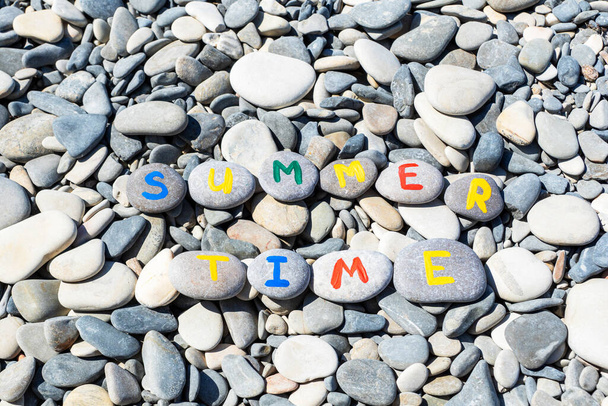 Inschrift Sommerzeit mit bunten Buchstaben geschrieben auf Steinen, die auf grauen Steinen liegen Hintergrund. Kreative Idee, Sommerzeit-Konzept. - Foto, Bild