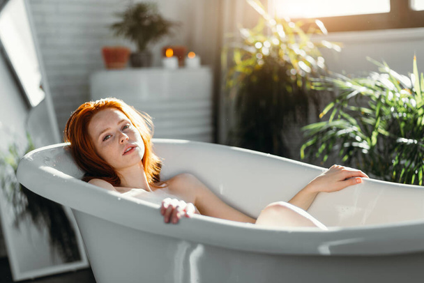Red-haired woman relaxing in bathtub with foam in spa center. - Foto, Imagem