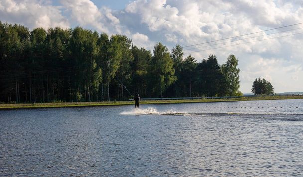 Silueta de esquí acuático moviéndose rápido en salpicaduras de agua al atardecer - Foto, imagen