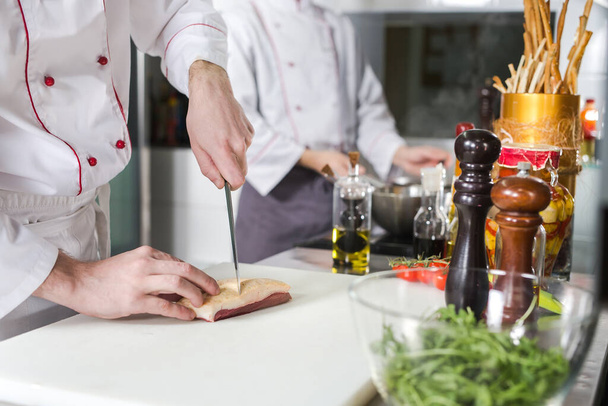 Chef cutting meat on chopping board, professional cook holding knife and cutting meat in restaurant. - Photo, Image