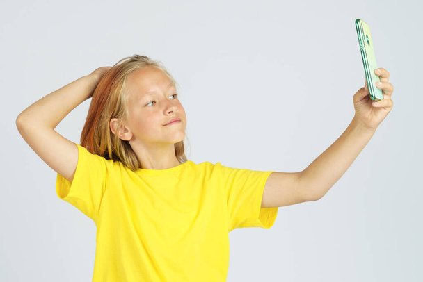 A teenage girl in a yellow T-shirt takes a selfie on a mobile phone. Isolated background. Education concept. - Fotoğraf, Görsel