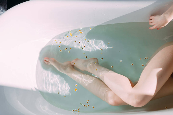 Cropped shot of female slim legs in bathtub with clean water and little flowers - Foto, immagini