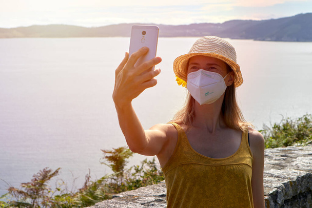 見張り所でスマホで自撮りする顔保護マスクの若い女。新しい通常の概念. - 写真・画像