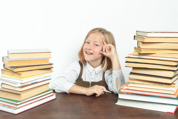 Portrait of a teenage girl, at a table among the books. Looks at the camera happily. Education concept. - Foto, Bild