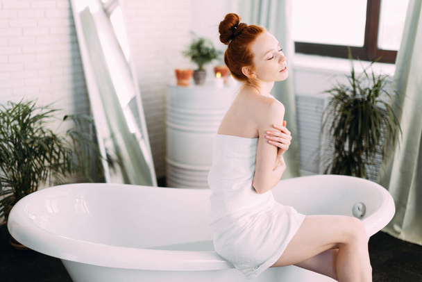 Redhead woman preparing foam bath in spacious bathroom with green plants - 写真・画像