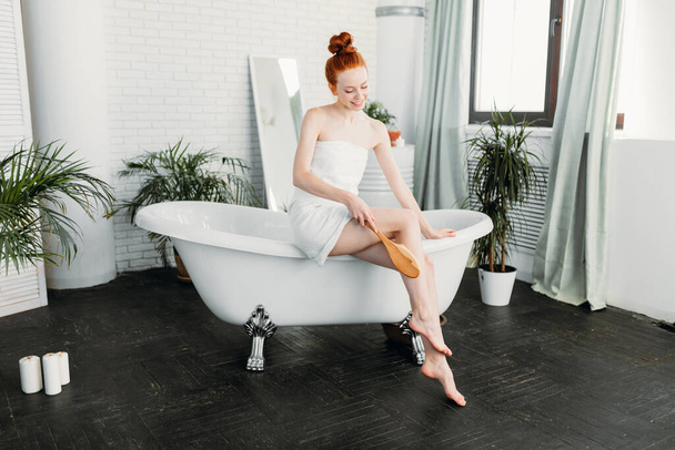 Redhead woman preparing foam bath in spacious bathroom with green plants - Foto, Bild