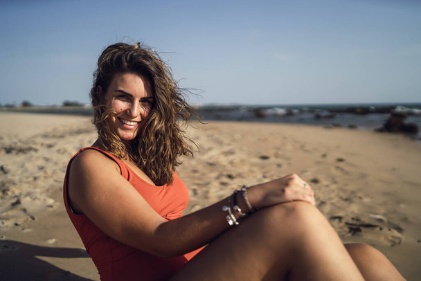 A pretty female sitting on Rota beach, Spain, wearing a swimsuit during a windy day - Zdjęcie, obraz