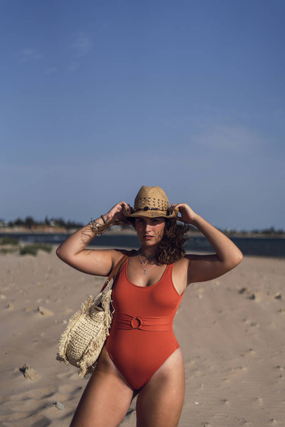 A vertical shot of a beautiful female wearing a swimsuit and a hat on Rota beach, Spain during a windy day - Фото, изображение
