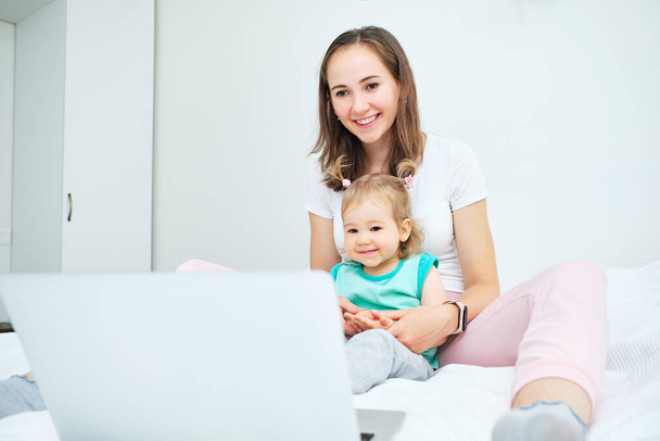 Portrait of happy caucasian child and mom sitting on sofa and watching video on laptop. - Photo, Image