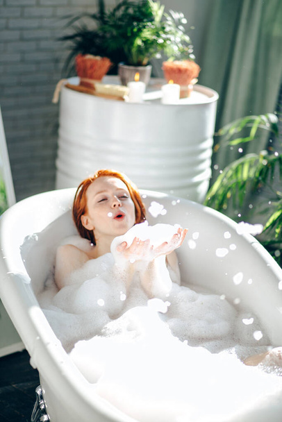 Portrait of happy young woman playing with foam in bathtub - 写真・画像
