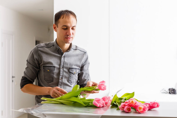 Mann Florist macht roten Tulpenstrauß und Verpackung in Packung auf Holztisch. Blumen - Foto, Bild