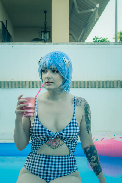 A shallow focus shot of a European female with blue hair covered in tattoos enjoying herself at the pool - Zdjęcie, obraz