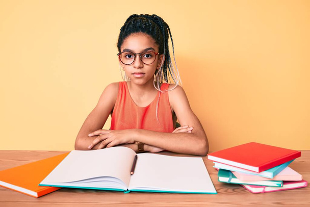 Jong Afrikaans-Amerikaans meisje met vlechten die studeren voor een schoolexamen met een serieuze uitdrukking op het gezicht. eenvoudig en natuurlijk kijkend naar de camera.  - Foto, afbeelding