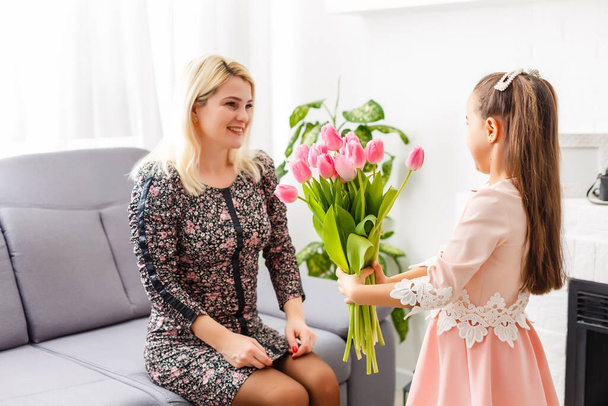 Gelukkige moederdag. Kind dochter feliciteert moeders en geeft haar bloemen tulpen - Foto, afbeelding